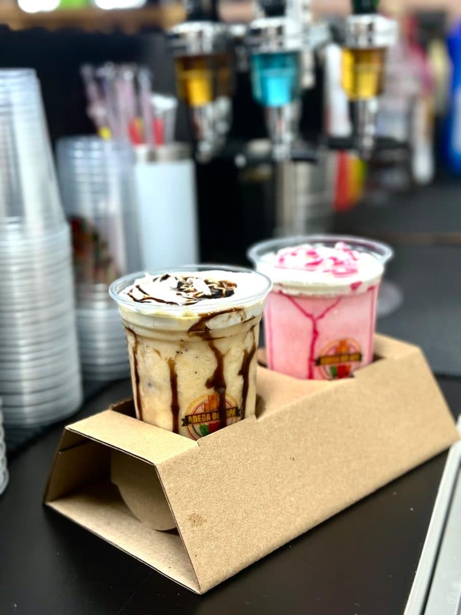 Dois copos cremosos de chocolate e rosa em suporte de papelão, no balcão da adega